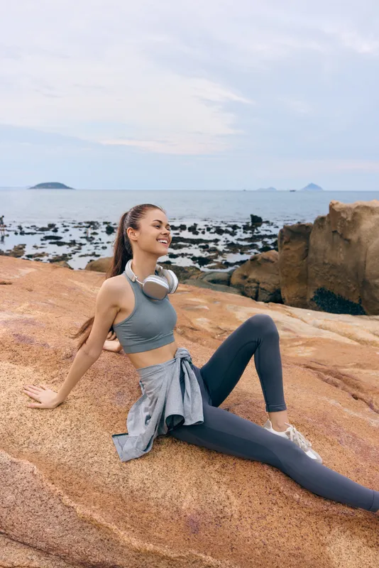 Young woman enjoying the seaside in sports attire, smiling and relaxed, showcasing healthy lifestyle and fitness concept by the ocean