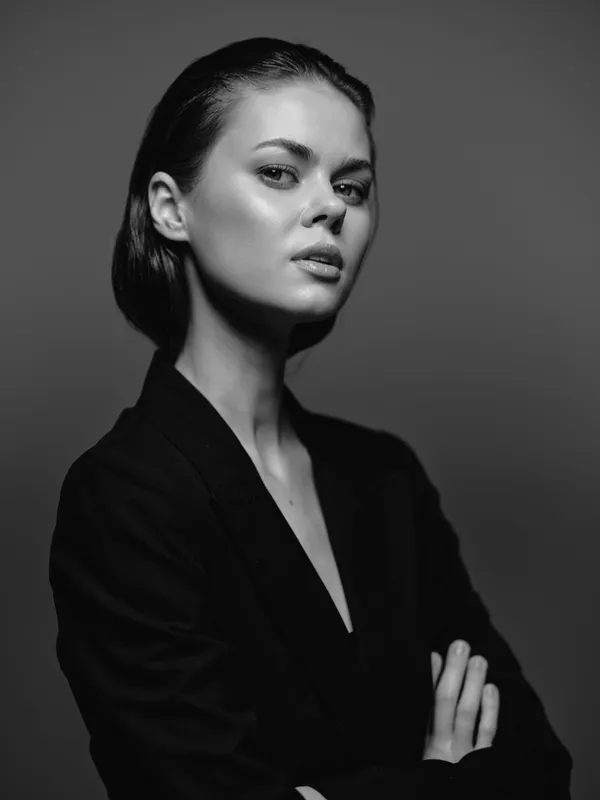 Black and white portrait of confident woman with crossed arms in stylish blazer, expressing elegance and strength in studio lighting.