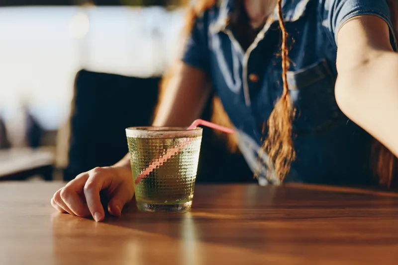 lifestyle woman in modern boho-western denim street style holding glass with straw, natural light and warm film color tone creating relaxed mood