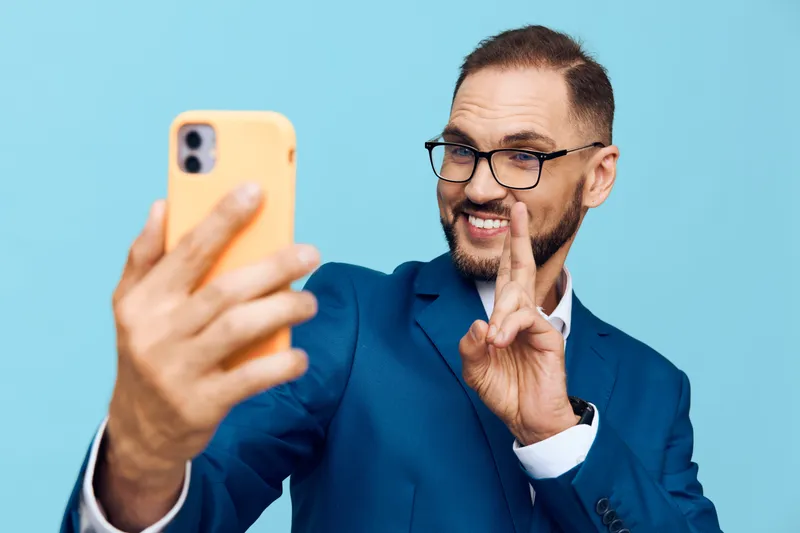 A professional man in a blue suit poses for a self portrait against a solid blue background, exuding confident, approachable energy and business style.