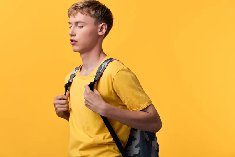 Young student with a backpack stands against a vibrant yellow backdrop, casual outfit, ready for classes, travel or daily learning, showing curiosity and energetic mood, contemporary lifestyle