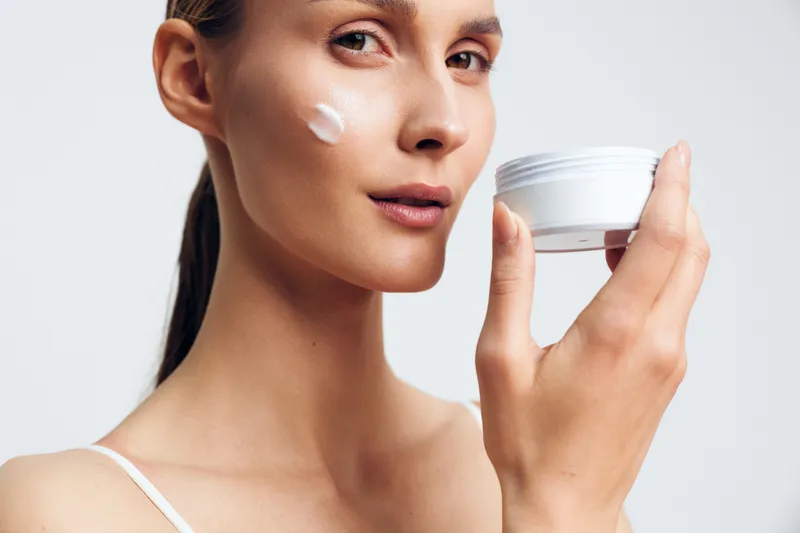Woman applying face cream from a jar, close up on skin, studio lighting, skincare self care, wellness beauty concept, smooth complexion, clean light background, calm mood