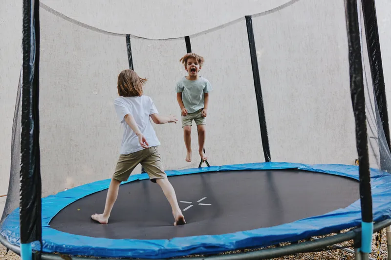 Happy children jumping on a trampoline, enjoying their time outdoors while having fun under the clear blue sky in a playful atmosphere.