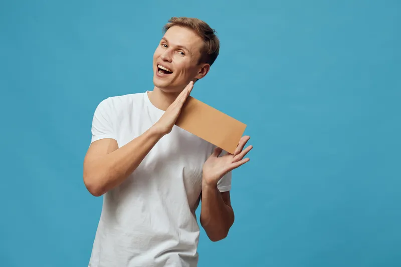 Smiling happy young man with short hair wear white t-shirt hold cardboard box in hand look camera isolated on blue background studio portrait. People lifestyle concept