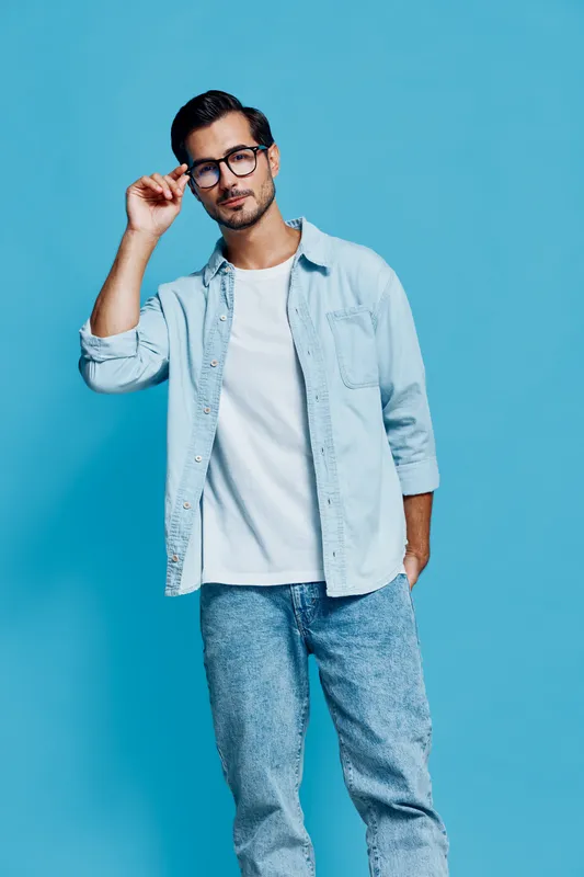 Full body stylish young man wearing glasses poses confidently against a vibrant blue background, showcasing a relaxed yet trendy outfit. Fashion lifestyle concept.