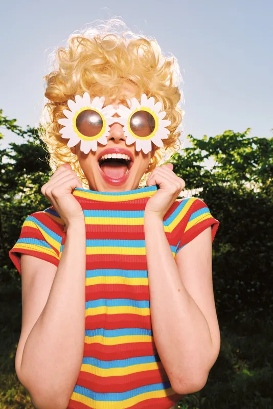 A playful figure wearing a bright striped shirt and flower sunglasses enjoys a sunny outdoor moment, capturing retro lifestyle, cheerful whimsy, bold, colorful joy.