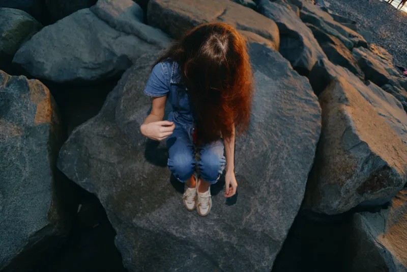 lifestyle woman in modern boho-western denim sitting on large rocks outdoors in warm film color tones representing relaxed street style mood