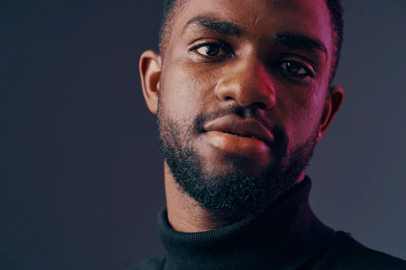 Portrait of a young Black man wearing a turtleneck sweater, showcasing confidence and thoughtfulness against a moody, colorful background