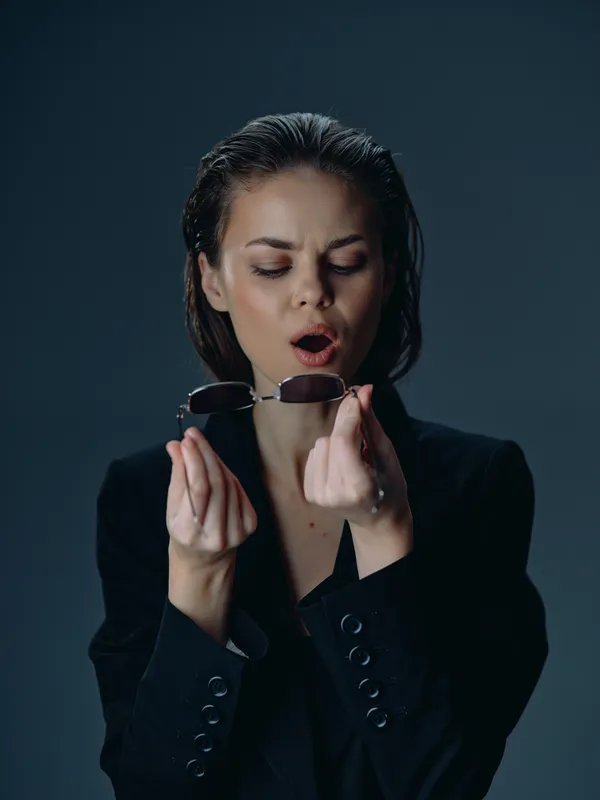 surprised woman holds sunglasses in dark background with moody lighting