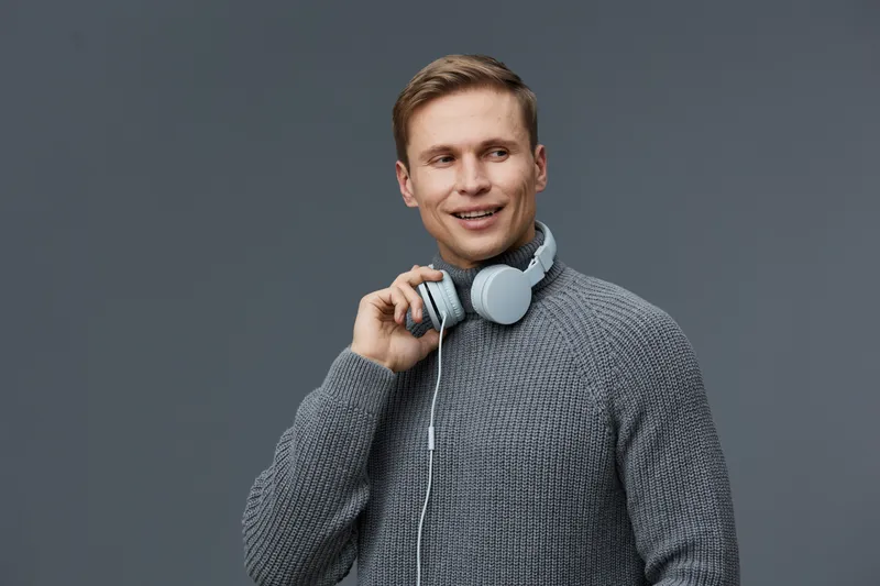 smiling young caucasian man wear grey sweater hold headphones look side isolated on dark grey background digital detox mental health concept