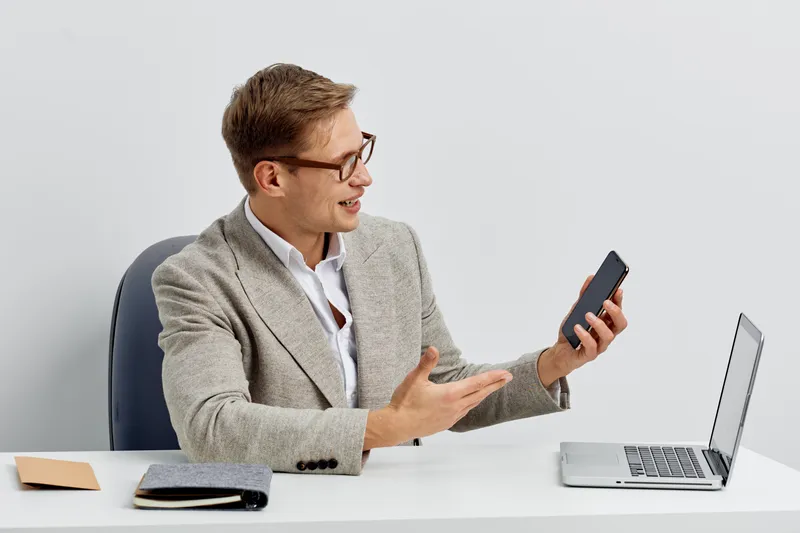 Young caucasian man working with smartphone laptop digital nomad remote communication casual wear glasses sitting office desk white background