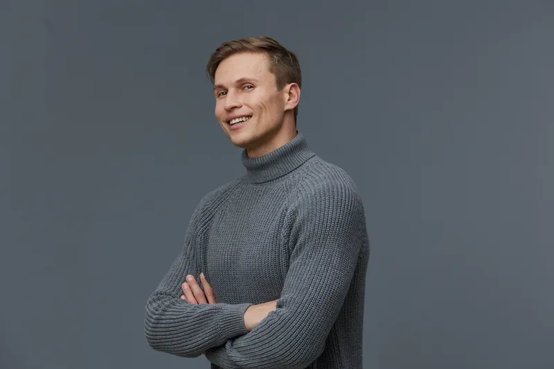 Confident smiling man with light brown hair wearing cozy gray turtleneck sweater standing against plain gray background studio portrait, casual style, cheerful expression, portrait photography, people
