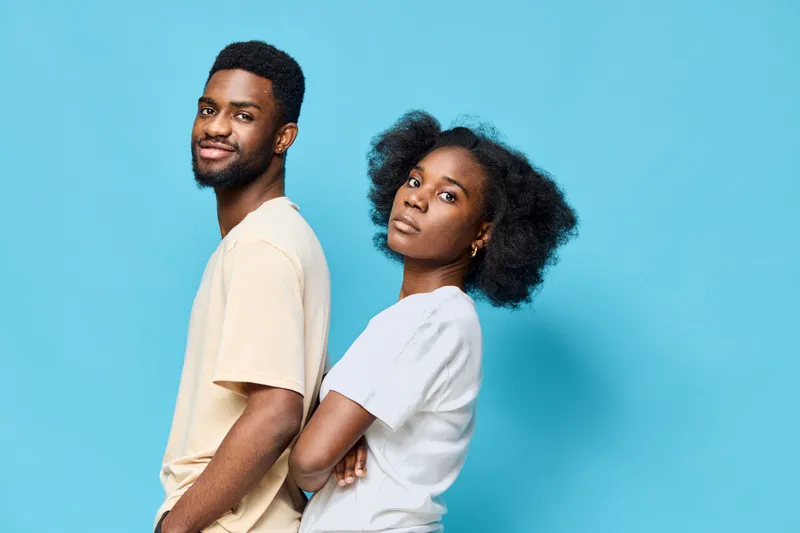 Young diverse couple in casual outfits against a bright blue background, showcasing confidence and style with modern fashion trends