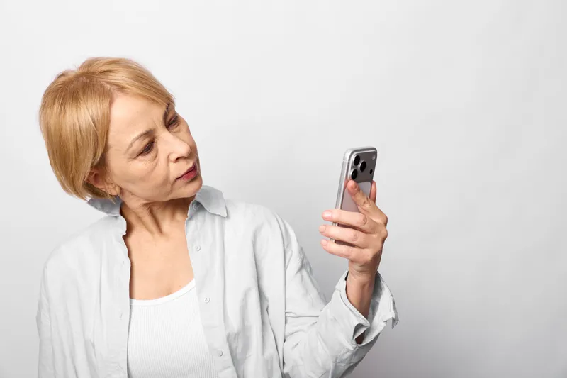 Elderly woman in white, stressed and anxious, holds a smartphone and looks worried, in healthcare, loneliness and mental health, emotional strain, communication concept alone today