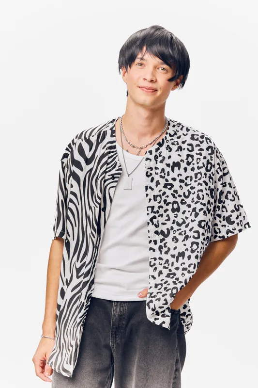 young man wearing black and white animal print shirt with casual jeans smiling confidently against white background, contemporary fashion style