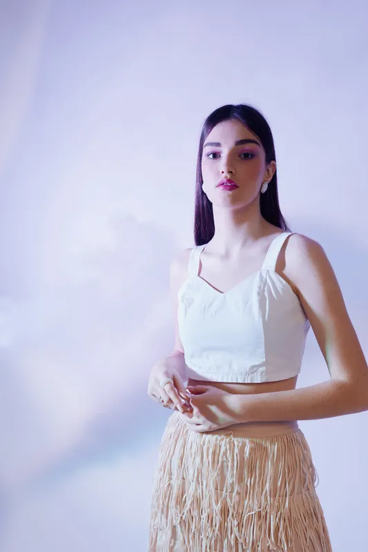 Young woman beauty fashion model poses in white top and beige fringe skirt against soft purple background. Studio portrait with elegant expression and stylish look. Concept for style.