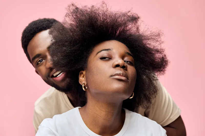 A joyful couple with natural hairstyles against a pink background, highlighting self expression and love, perfect for showcasing diversity and individuality
