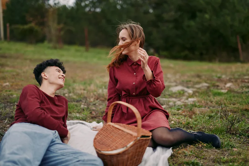 Young couple relaxing on a picnic blanket in a grassy meadow, sharing a candid moment with genuine smiles and natural interaction that conveys authenticity, quiet reliability and heartfelt connection.