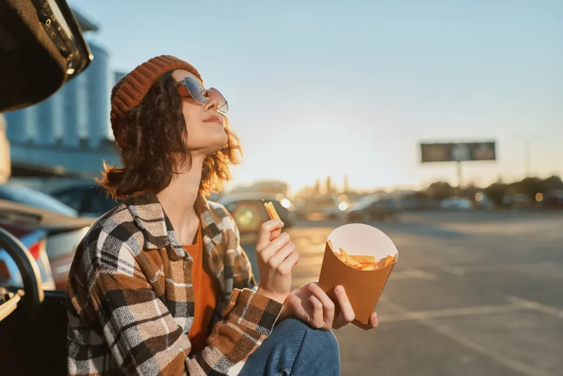 woman fries car sunset beanie sunglasses parking casual enjoying golden hour glow with authenticity and candid lifestyle vibe, mindful living and emotional storytelling in urban roadside scene