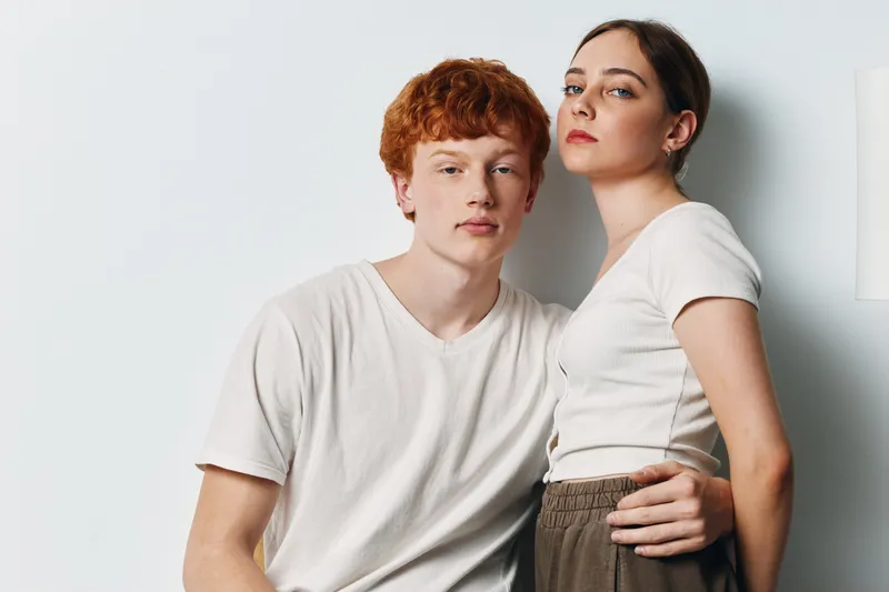 Young man and woman posing together in casual clothing against plain background. They show confident expressions with close body contact and modern style for portrait photography.
