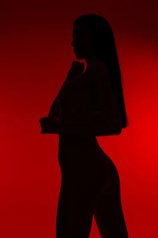 Silhouette of a woman sport fitness posing against a red background, showcasing strength and elegance with a minimalistic and dramatic lighting style.
