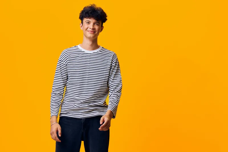 smiling man wearing striped shirt standing confidently against vibrant orange background with casual style and relaxed mood, youthful and modern atmosphere