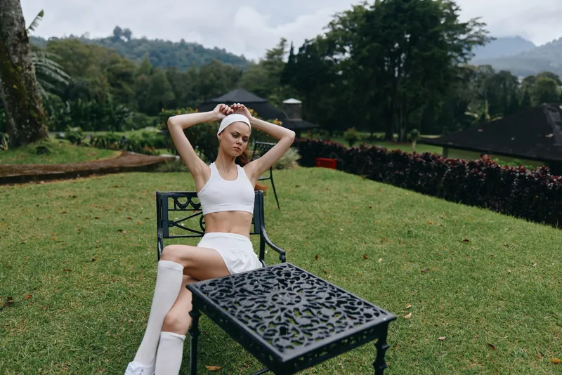 Young woman in stylish activewear practicing yoga outdoors, showcasing wellness and relaxation in a serene green environment, while exuding confidence and tranquility