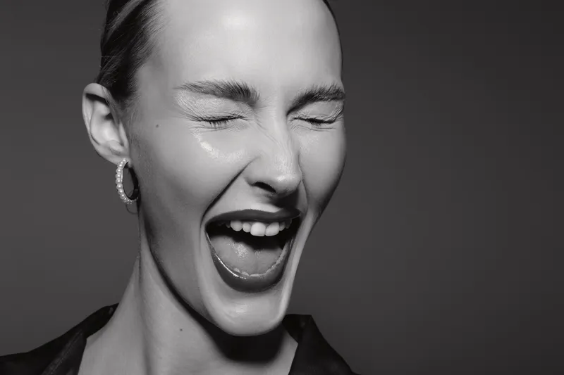 Close-up of a happy white woman with pale skin laughing with eyes closed in black and white studio portrait. Concept of joy, emotion, and natural expression.