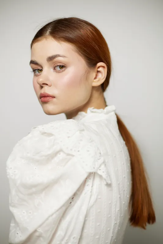Elegant young woman with long brown hair in a vintage white blouse, showcasing a serene expression against a neutral background Perfect for fashion or beauty concepts