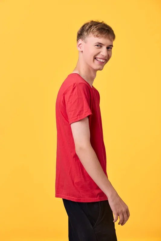 Smiling man in a red shirt stands against yellow backdrop, a studio shot capturing upbeat mood and confidence, suitable for lifestyle or ecommerce campaigns.