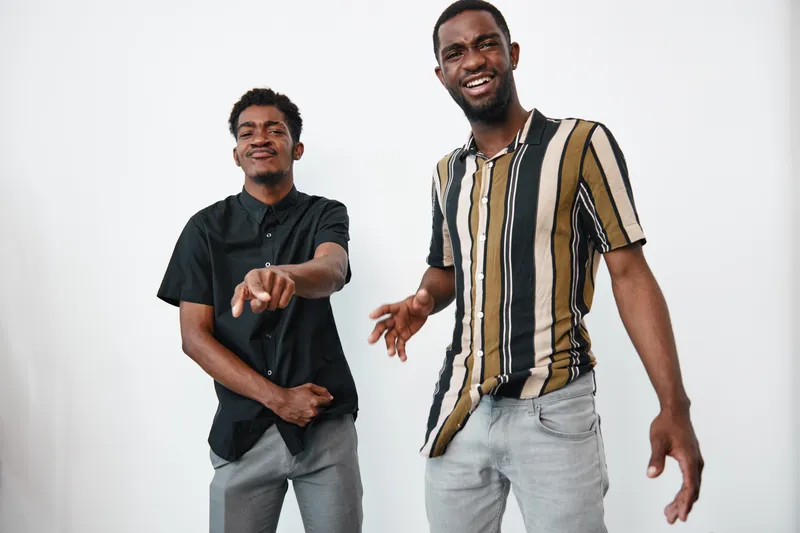 Two young African American men with dark skin smiling and dancing together in casual clothes against white background. Friendship, joy and positive energy in studio.