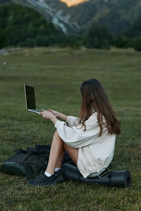 A focused individual sits on a grassy field outdoors, typing on a laptop. The scene conveys remote work, concentration, and a calm, productive atmosphere suitable for creative projects and flexible