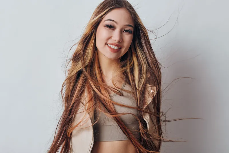 Young woman with long hair smiling and posing against white background for portrait, natural beauty and casual fashion with confident expression and modern style.