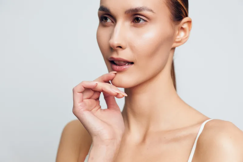 Woman skincare face close up beauty touching lips natural glow, bare shoulders, smooth skin, calm expression, minimal clean background, soft studio lighting, wellness mood, portrait