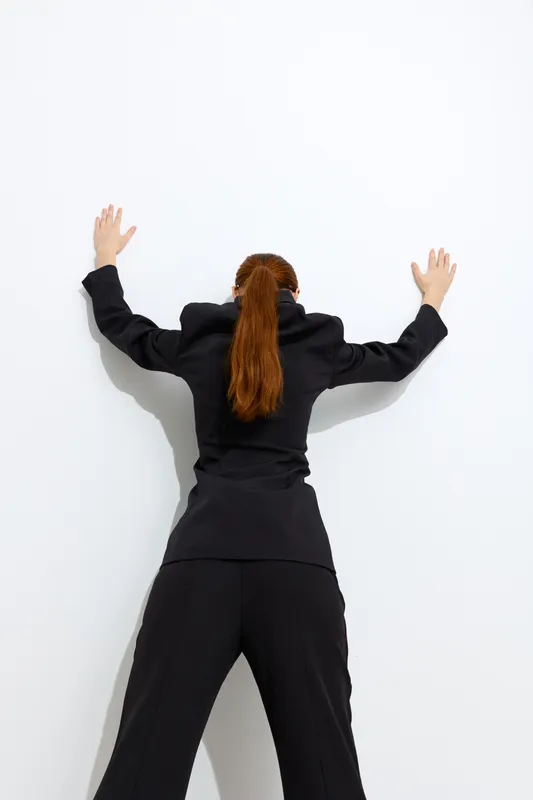 Fashion woman with long red hair wearing black outfit seen from behind against white background, showcasing modern style and minimalist design.