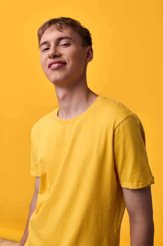 Smiling youth in a yellow tee against a vibrant backdrop, highlighting casual style, confidence, and a cheerful, sunny mood.