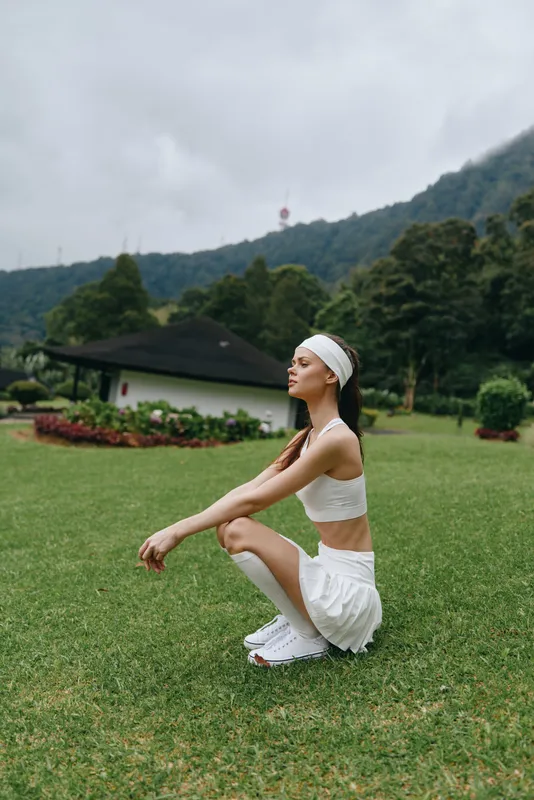 Young female model in sportswear squatting on the grass, conveying motivation and health, perfect for fitness, summer, or active lifestyle concepts