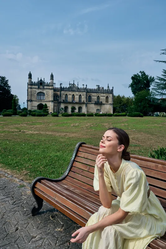 Woman on bench in park with historic mansion background, relaxation in sunlight, authenticity inclusivity