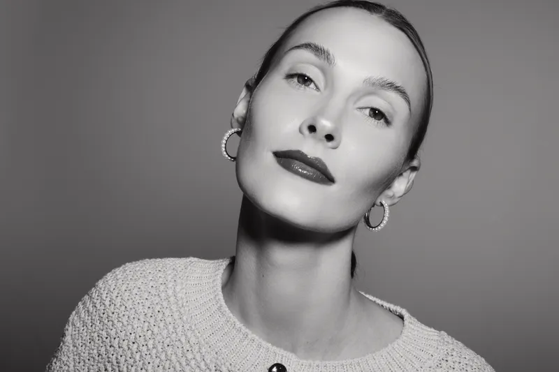 Portrait of a fair skinned Caucasian woman with slicked back hair and hoop earrings wearing knitted sweater in studio. Concept of beauty and fashion.