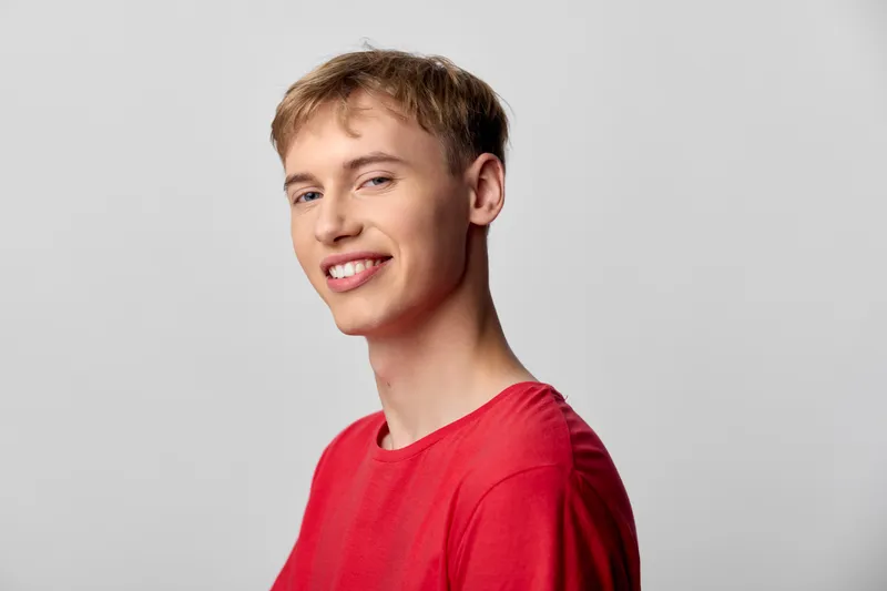 Smiling individual in a bright red shirt stands against a neutral backdrop, conveying confidence, approachability and casual style ideal for fashion, lifestyle or stock photography