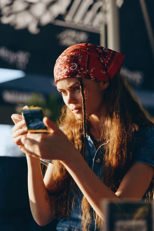 lifestyle woman with red bandana in modern boho-western denim street style using mirror with natural film color light and thoughtful expression
