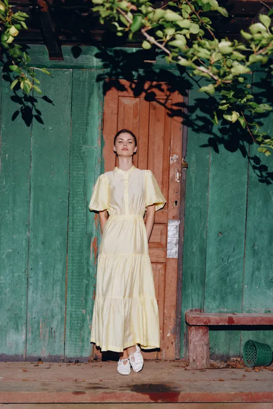 woman dress doorway rustic wooden green portrait yellow, authentic inclusive portrait of woman in vintage dress standing at weathered wooden house door with foliage and light