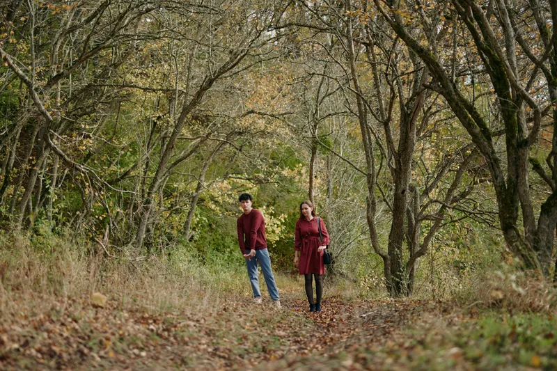 An authentic, candid moment as a couple walks along a leaf strewn forest path, captured in natural light with a real, unposed atmosphere and gentle connection.