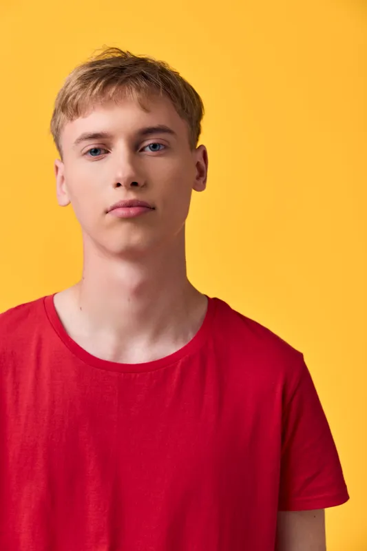 Young man in a red shirt against a bright yellow background, studio shot, casual fashion, head and shoulders view, minimalist lighting, clean backdrop for a modern lifestyle image.