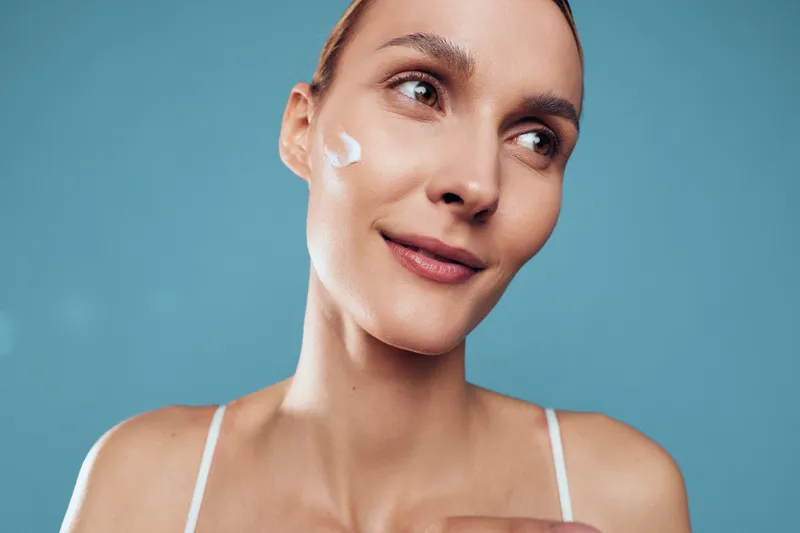 Woman with skincare cream on face, close up portrait on blue background, beauty routine concept, fresh hydrated skin, self care and wellness, soft studio lighting