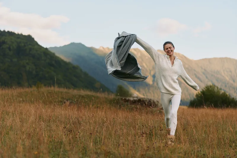 Joyful woman running in an open field with a flowing scarf, capturing carefree outdoor lifestyle and nature energy, wind lifting fabric in warm sun and vibrant sunlit mood.
