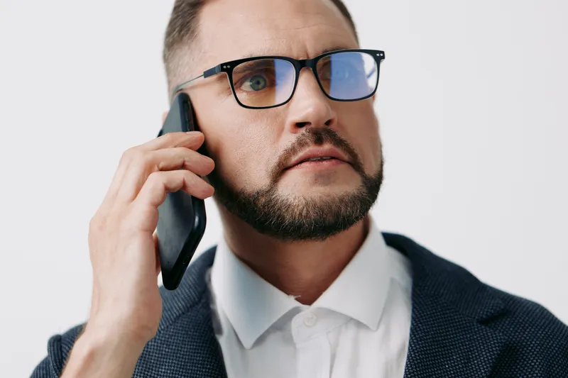A focused business professional man on a solid colored background, speaking on a mobile phone with intent and confident expression, conveying leadership and concentration.