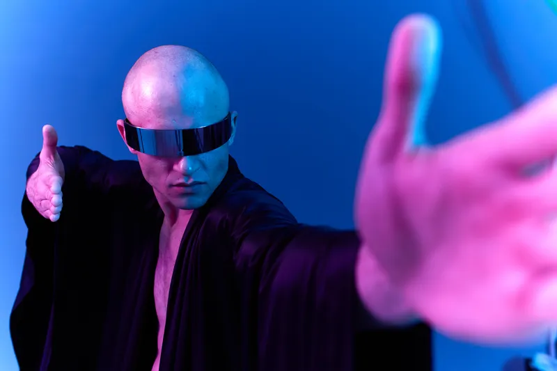 A man in futuristic attire with sunglasses strikes a dynamic pose, exuding confidence and mystery. The vibrant blue and purple lighting enhances the image's atmosphere.