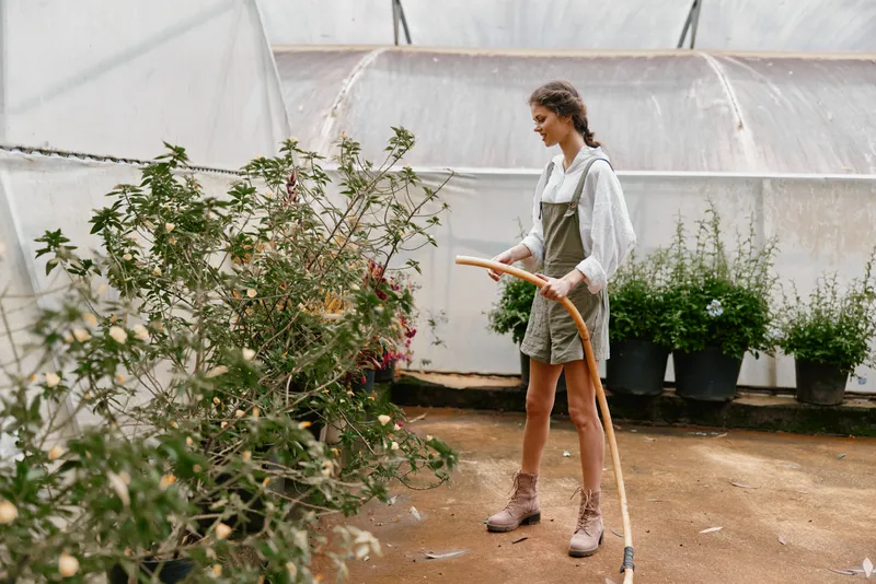 Young woman watering plants in a greenhouse, wearing a casual outfit and displaying a joyful expression, showcasing a connection to nature and sustainable gardening