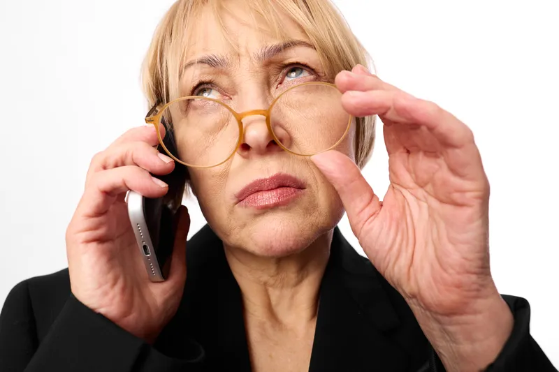 Woman senior phone eyeglasses portrait indoors communication glasses, thoughtful face holding glasses near eyes, studio white background, calm quiet moment